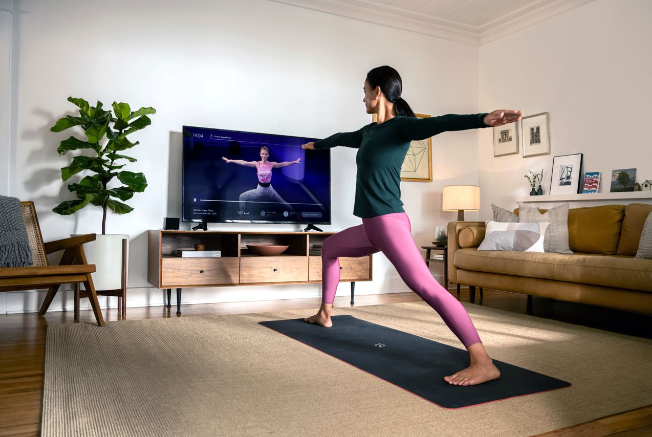 Woman in workout clothes in a yoga pose, matching a person posing on the tv in front of her.